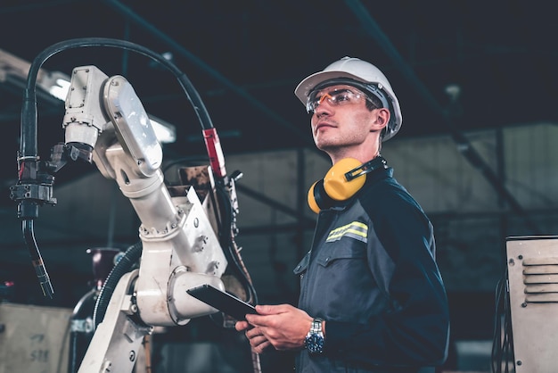 Giovane operaio di fabbrica che lavora con un abile braccio robotico