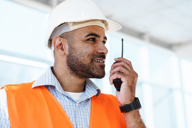 Giovane operaio edile in uniforme che utilizza un walkie-talkie sul posto