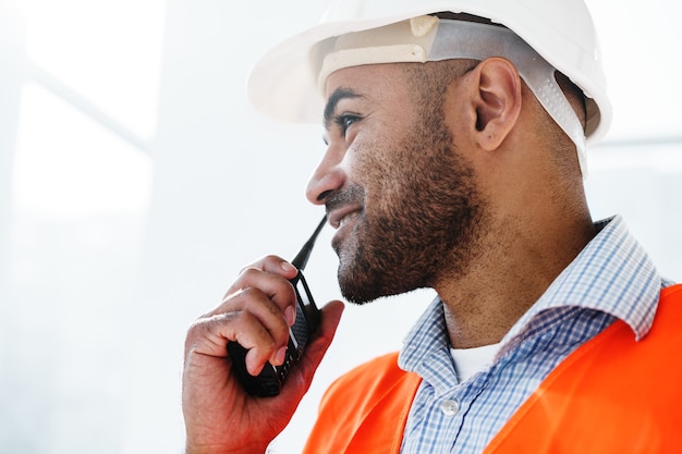 Giovane operaio edile in uniforme che utilizza un walkie-talkie sul posto