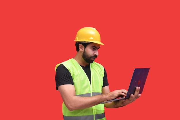 giovane operaio edile utilizzando laptop su sfondo rosso modello pakistano indiano