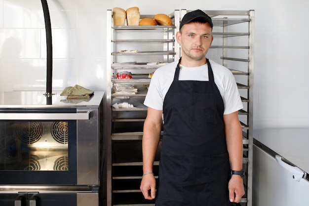 Giovane operaio panettiere in una panetteria in uniforme