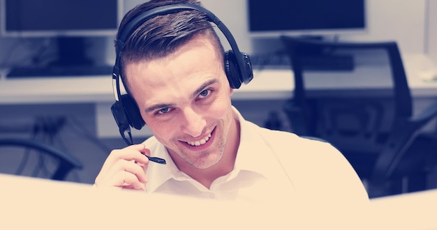 giovane operatore di call center maschio sorridente che fa il suo lavoro con un auricolare