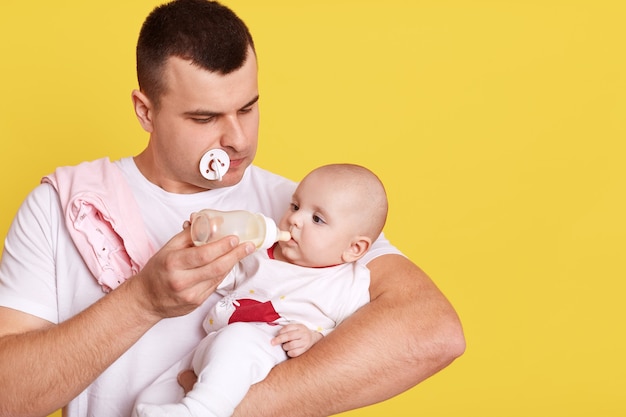 Giovane padre bello che alimenta il suo figlio neonato con il latte dal biberon