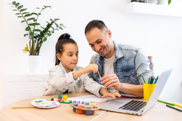 Giovane padre che aiuta sua figlia con il suo progetto scolastico sul laptop a casa