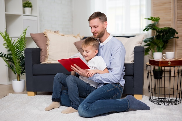 Giovane padre che legge un libro al suo piccolo figlio carino a casa