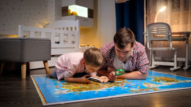 Giovane padre con figlio piccolo che esplora e guarda sulla mappa attraverso la lente di ingrandimento. Concetto di viaggio, turismo e educazione dei bambini.