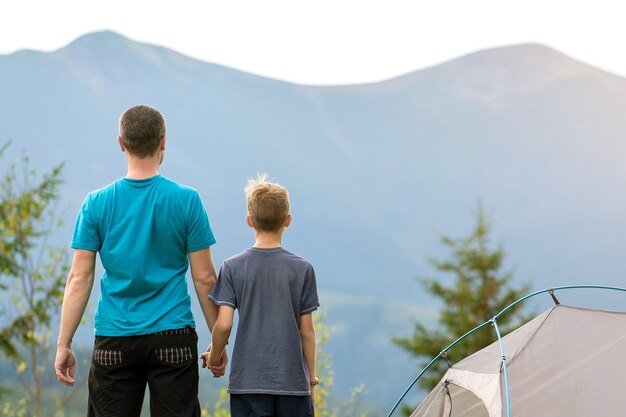 giovane padre con suo figlio figlio in piedi insieme vicino a una tenda da escursionista in montagna estiva.