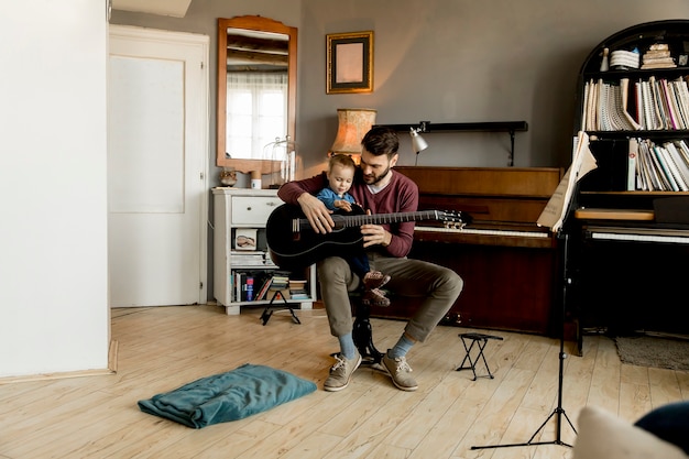 Giovane padre e piccola figlia che giocano chitarra acustica nella stanza a casa