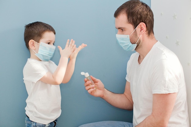 Giovane padre e suo figlio bambino che usano un disinfettante per le mani su sfondo blu