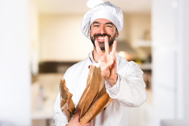 Giovane panettiere che tiene un po &#39;di pane e contando tre in cucina