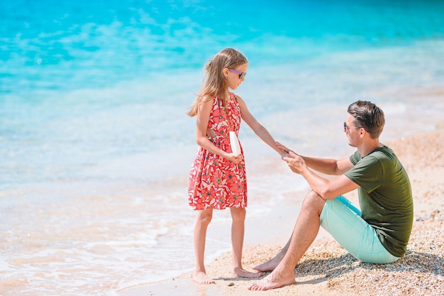 Giovane papà che applica la crema solare al naso della figlia sulla spiaggia. protezione solare