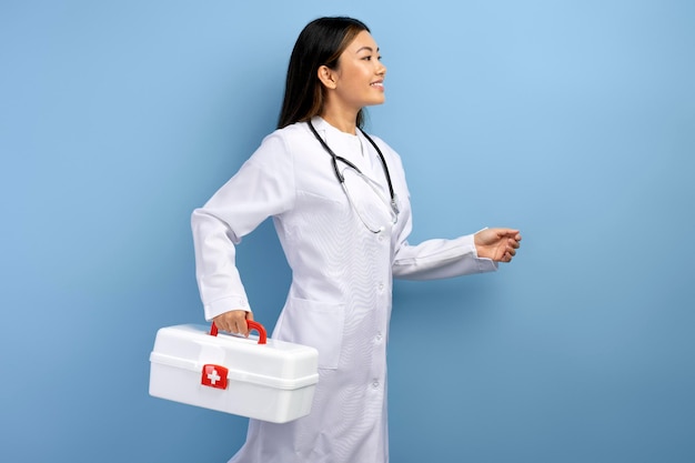 Giovane paramedico asiatico in uniforme bianca che corre con la scatola con la medicina