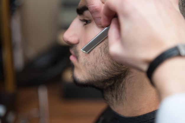 Giovane parrucchiere bello che dà un nuovo taglio di capelli al cliente maschio al salone