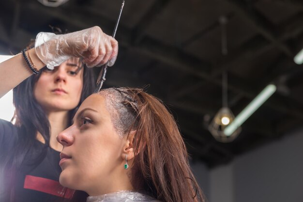 Giovane parrucchiere che tinge accuratamente i capelli della cliente mentre è seduta su una sedia nel salone di bellezza