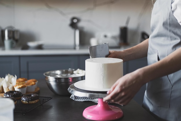 Giovane pasticcere donna adorabile che prepara una torta festiva a casa in cucina