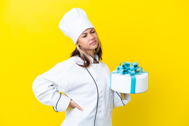 Giovane pasticcere russo donna con una grande torta isolata su sfondo giallo che soffre di mal di schiena per aver fatto uno sforzo