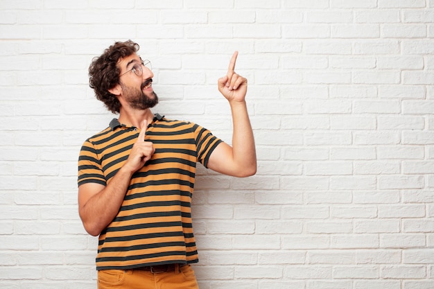 Giovane pazzo o uomo sciocco che gesturing e che esprime le emozioni contro il fondo del muro di mattoni