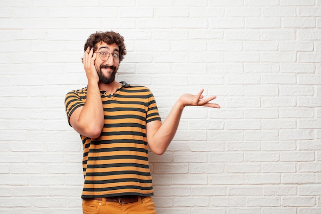 Giovane pazzo o uomo sciocco che gesturing e che esprime le emozioni contro il fondo del muro di mattoni