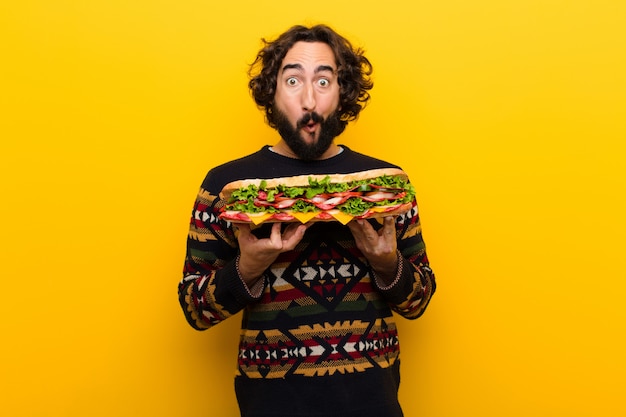 Giovane pazzo uomo barbuto con un panino gigante.