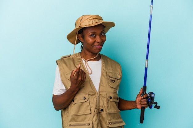 Giovane pescatrice afroamericana che tiene l'asta isolata su sfondo blu che punta con il dito su di te come se invitasse ad avvicinarsi.