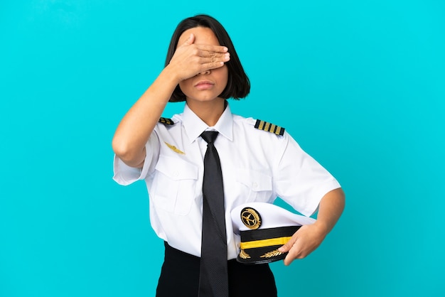 Giovane pilota di aeroplano su sfondo blu isolato che copre gli occhi con le mani