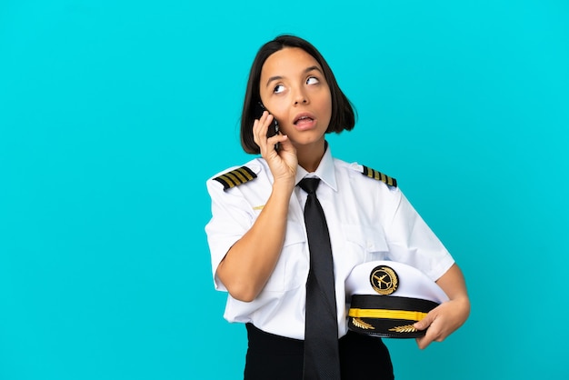 Giovane pilota di aeroplano su sfondo blu isolato mantenendo una conversazione con il telefono cellulare