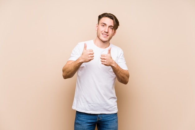 Giovane posa caucasica dell'uomo isolata sollevando entrambi i pollici in su, sorridendo e sicuro.