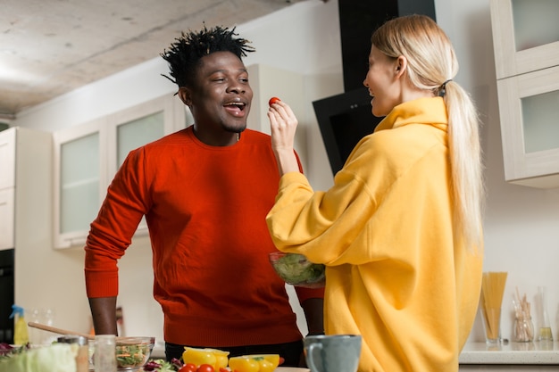 Giovane positivo che apre la sua bocca e la sua ragazza che lo alimenta con pomodorini