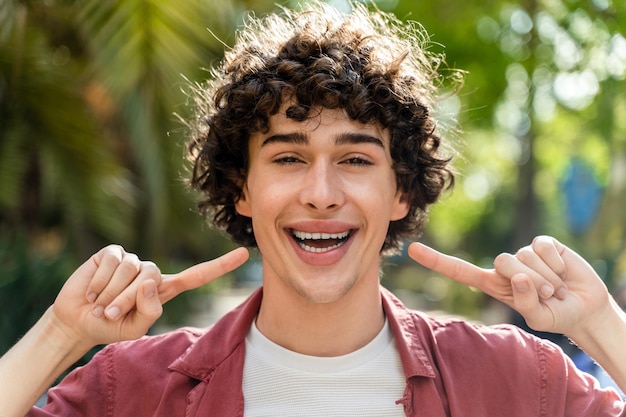 Giovane positivo che si copre le orecchie e sorride mentre posa al parco verde