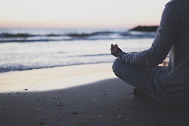 Giovane pratica yoga sulla spiaggia al tramonto.