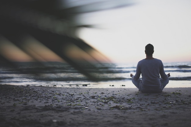 Giovane pratica yoga sulla spiaggia al tramonto.