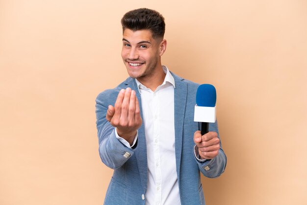 Giovane presentatore televisivo caucasico isolato su sfondo bianco che invita a venire con la mano Felice che tu sia venuto