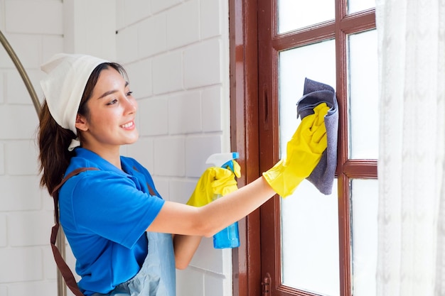 Giovane professionista asiatica di servizi di pulizia donna operaia che lavora in casa la ragazza pulisce la finestra di vetro
