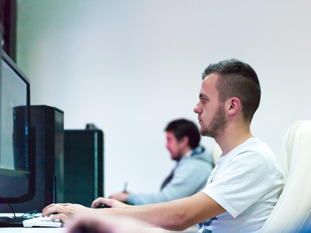 Giovane progettista grafico che lavora sul posto di lavoro. Ragazzo seduto a tavola ritoccando foto usando tablet digitale con penna e computer desktop all'interno. Concetto di lavoro freelance e a distanza