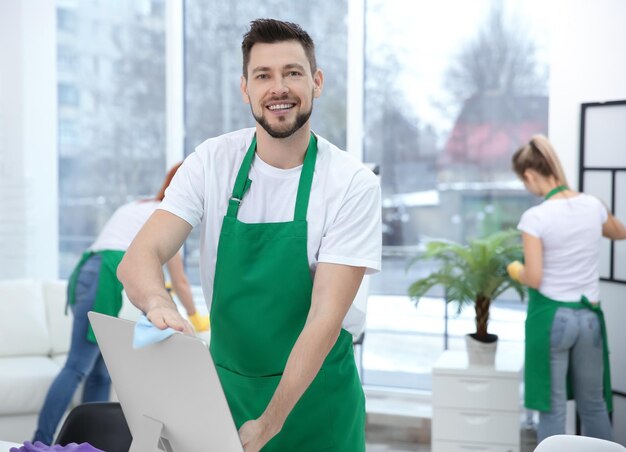 Giovane pulitore maschio che pulisce computer all'ufficio