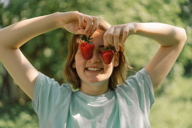 Giovane ragazza adolescente con la fragola in una maglietta in un esterno e guardando la telecamera la gente e la vita...