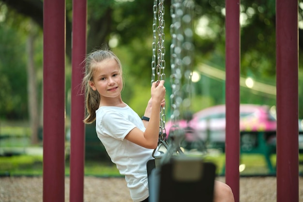 Giovane ragazza adolescente sorridente abbastanza felice che si diverte nelle oscillazioni del parco giochi durante le vacanze estive in una giornata di sole