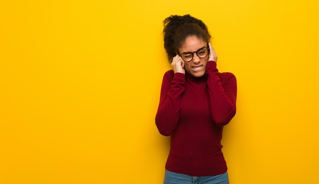 Giovane ragazza afroamericana nera con gli occhi azzurri che coprono le orecchie di mani