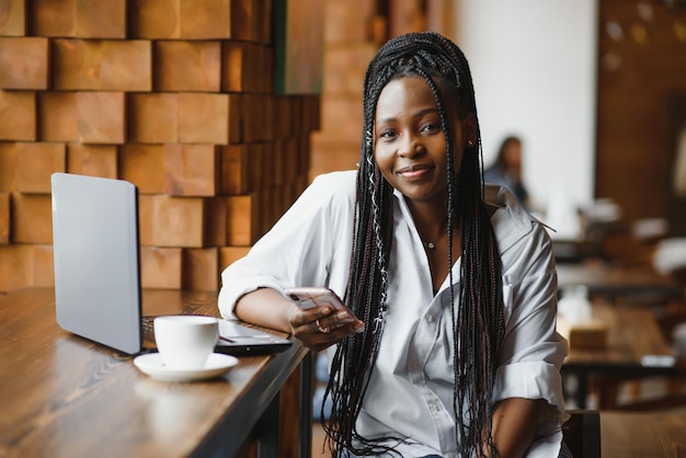 Giovane ragazza afroamericana seduta al ristorante e digitando sul suo computer portatile Bella ragazza che lavora al computer al bar