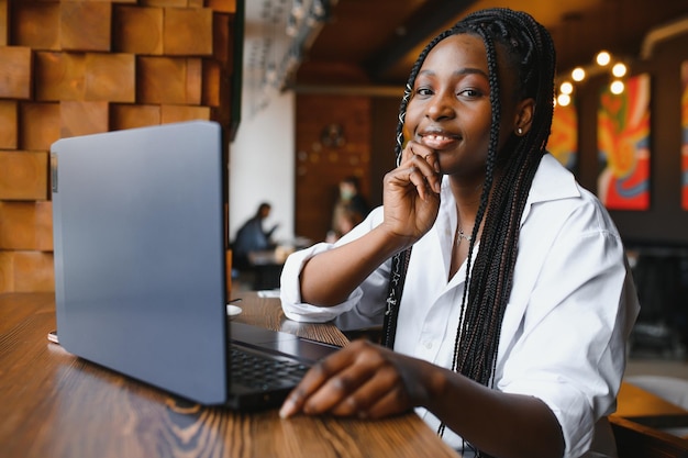 Giovane ragazza afroamericana seduta al ristorante e digitando sul suo computer portatile Bella ragazza che lavora al computer al bar