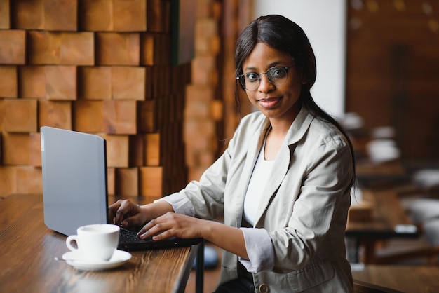 Giovane ragazza afroamericana seduta al ristorante e digitando sul suo computer portatile Bella ragazza che lavora al computer al bar