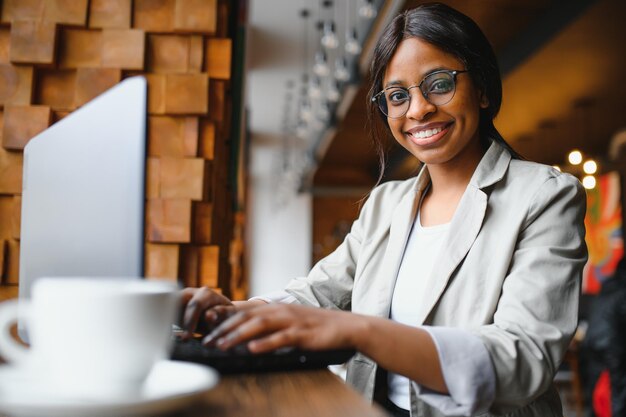 Giovane ragazza afroamericana seduta al ristorante e digitando sul suo computer portatile Bella ragazza che lavora al computer al bar