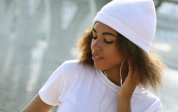Giovane ragazza afroamericana vicino al mare e al ponte utilizzando il telefono cellulare e lo stile di vita delle cuffie