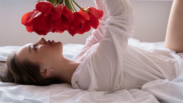 Giovane ragazza al mattino a letto con un mazzo di fiori di tulipani rossi per la festa della mamma festa della mamma donna nel primo piano della camera da letto