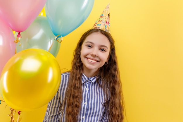 Giovane ragazza alla festa di compleanno con palloncini gonfiabili colorati isolati su una parete gialla