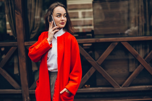 giovane ragazza alla moda in un cappotto rosso in piedi in una città d&#39;autunno