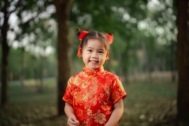 Giovane ragazza allegra con adorabili capelli rossi che indossa un vibrante vestito tradizionale cinese cheongsam all'aperto nel parco giardino concetto di giorno cinese