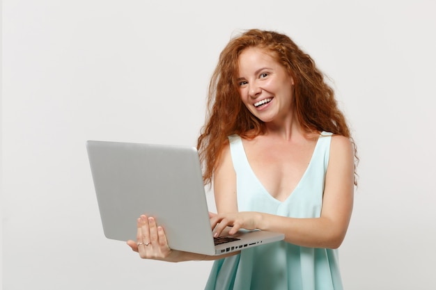 Giovane ragazza allegra della donna della testarossa in vestiti leggeri casuali che posano isolato sul ritratto bianco dello studio del fondo della parete. Concetto di stile di vita della gente. Mock up copia spazio. Tenendo lavorando sul computer pc portatile.