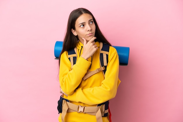 Giovane ragazza alpinista con un grande zaino isolato su sfondo rosa che ha dubbi