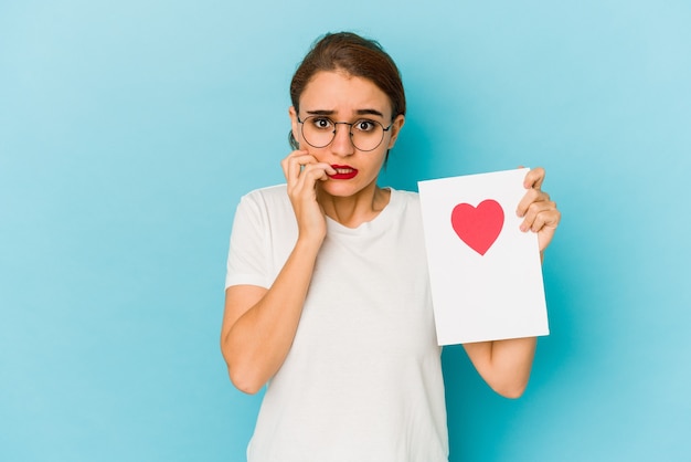 Giovane ragazza araba magra che tiene una carta di San Valentino che morde le unghie, nervosa e molto ansiosa.